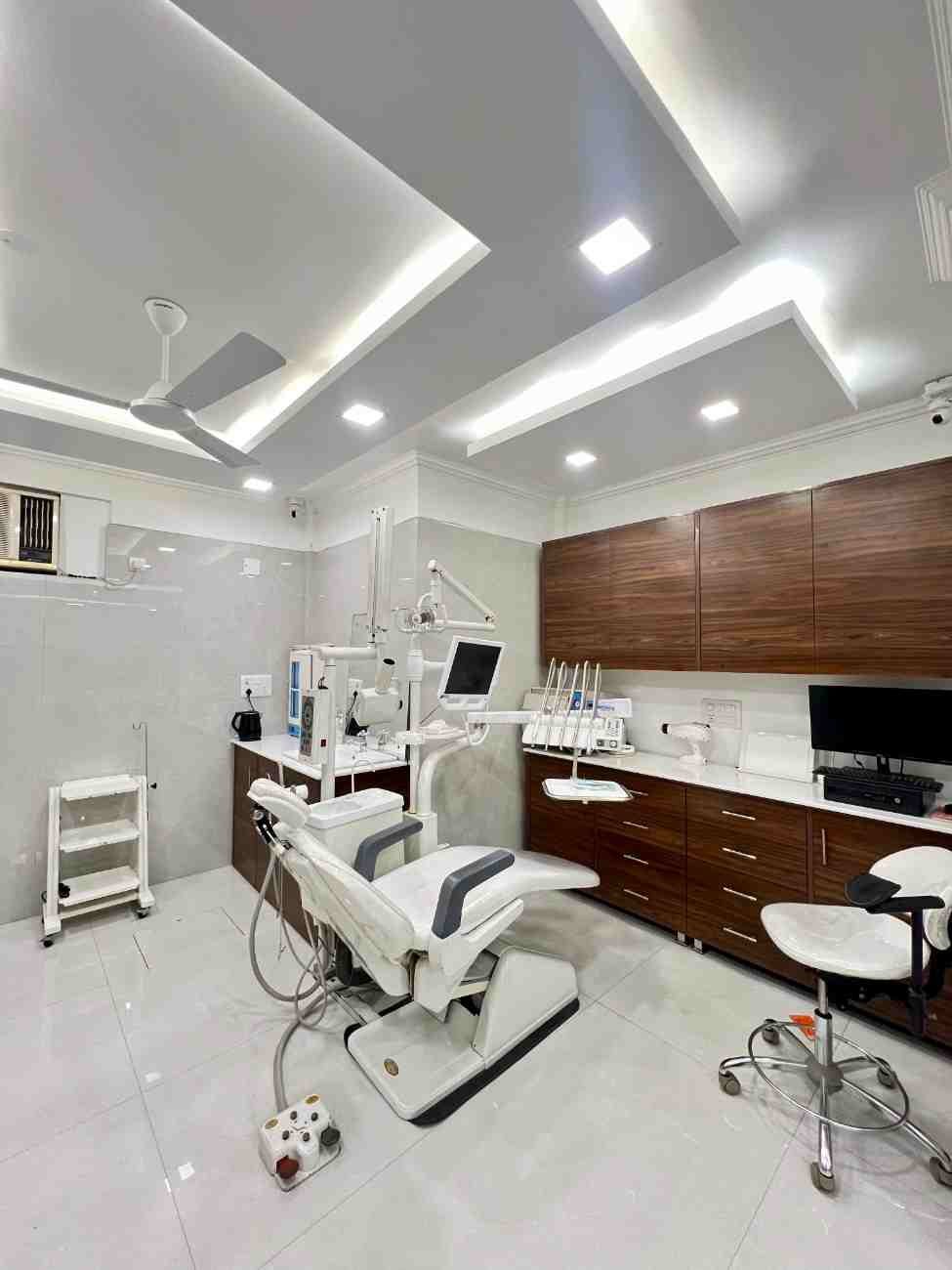 Clean dental operatory room with white dental chair, overhead light and wall-mounted monitor